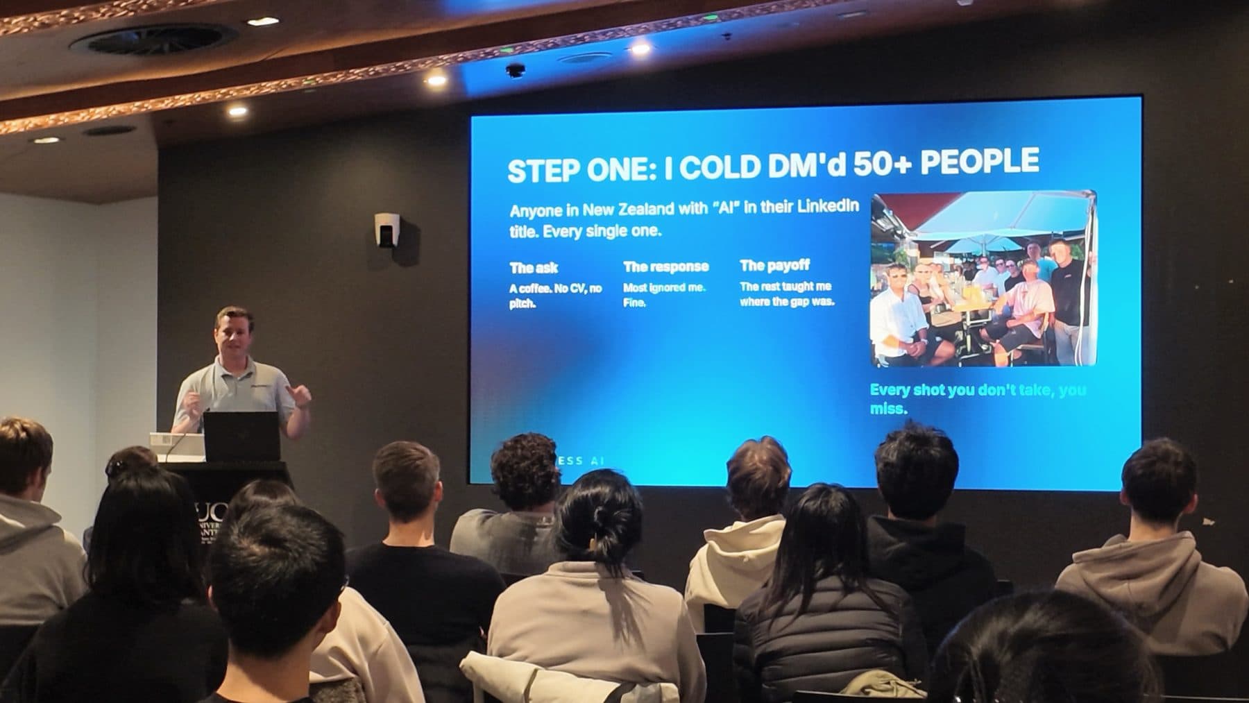 Blake Harkness speaking beside a slide reading "Step one: I cold DM'd 50+ people" at a student talk