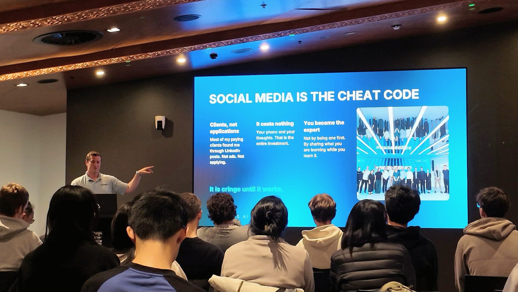 Blake Harkness gesturing to a slide reading "Social media is the cheat code" in front of a room of students