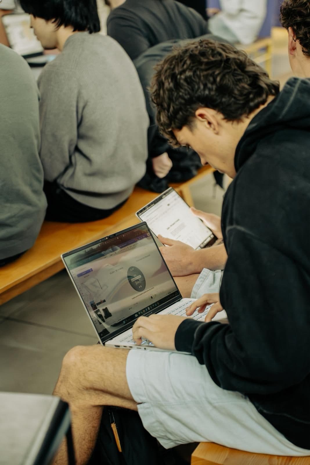 A SaaSathon competitor working on a laptop and tablet at a shared bench in Christchurch